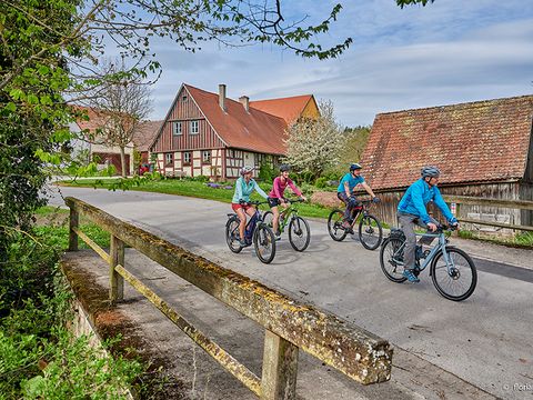 Eine Gruppe Radfahrer fährt an einem Bauernhof vorbei